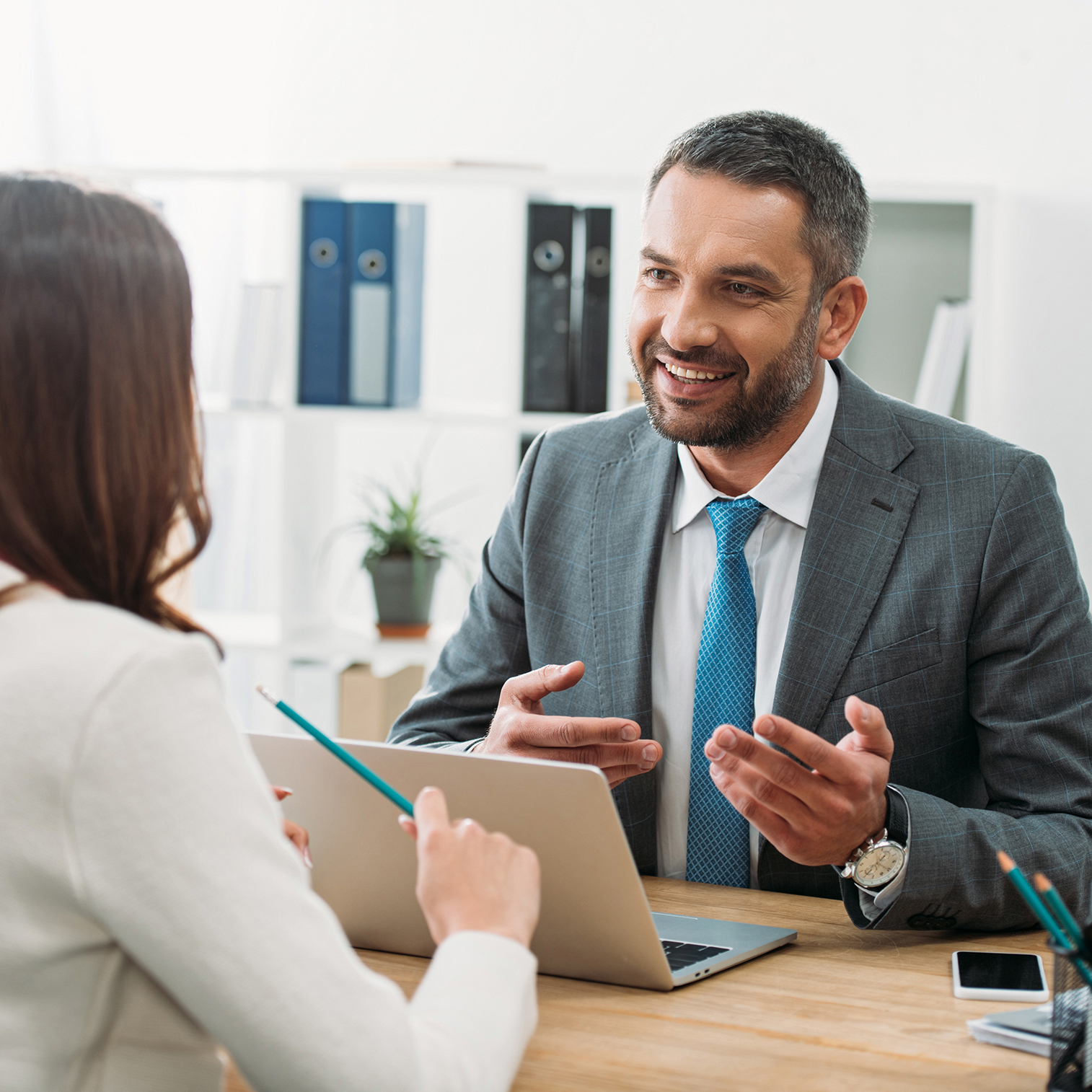 A professional man and woman speak to each other at a desk.