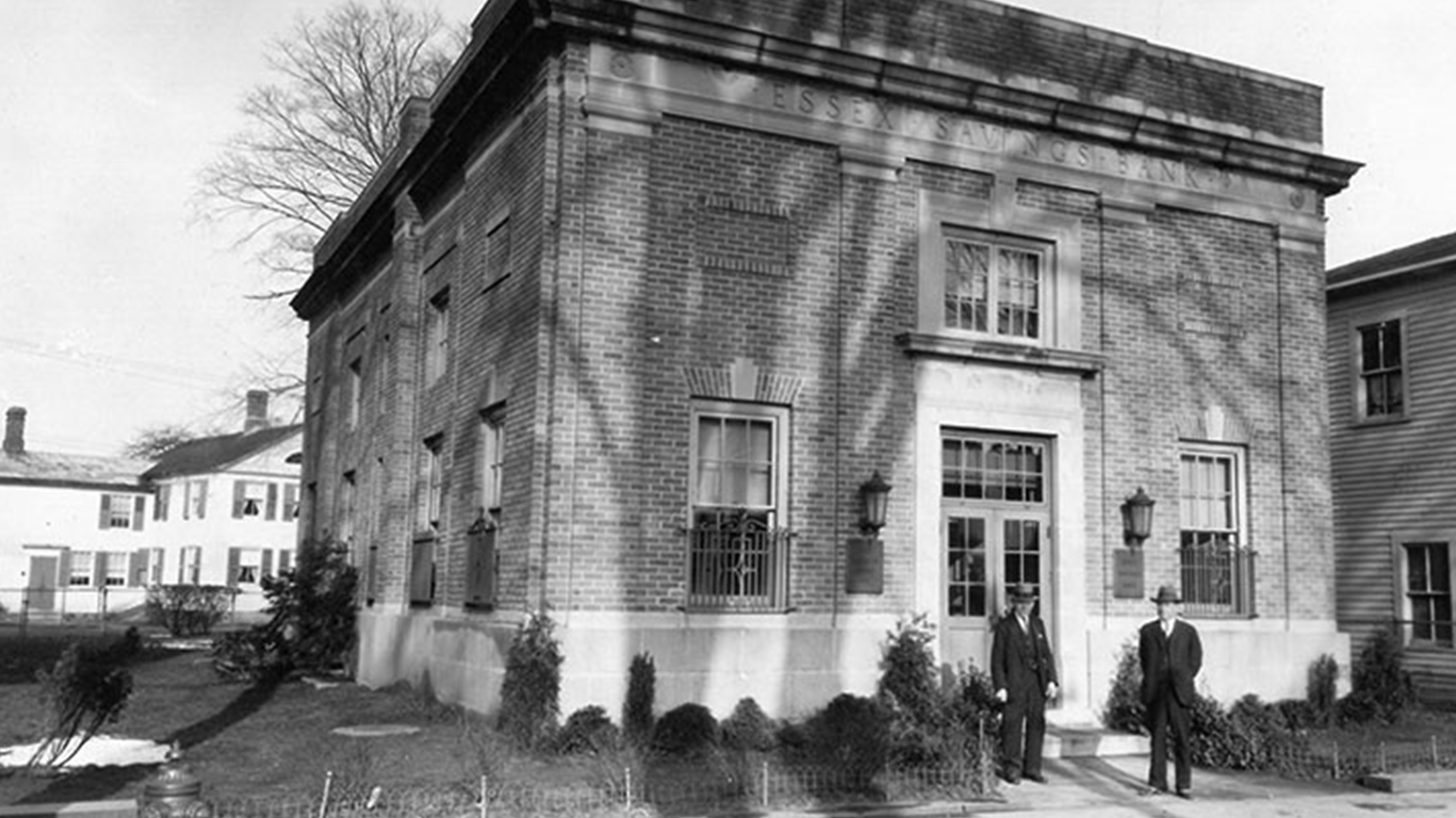 Old brick building, with two men standing right outside the door.