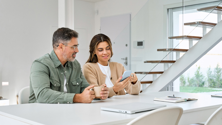 A couple is sitting together at a white table looking at phone and having a discussion