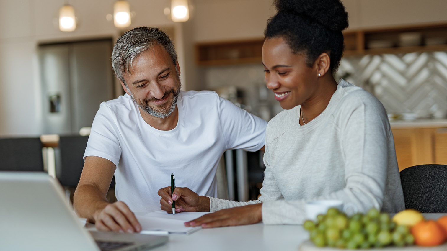 A man and a woman smiles while the woman writes on a notepad.