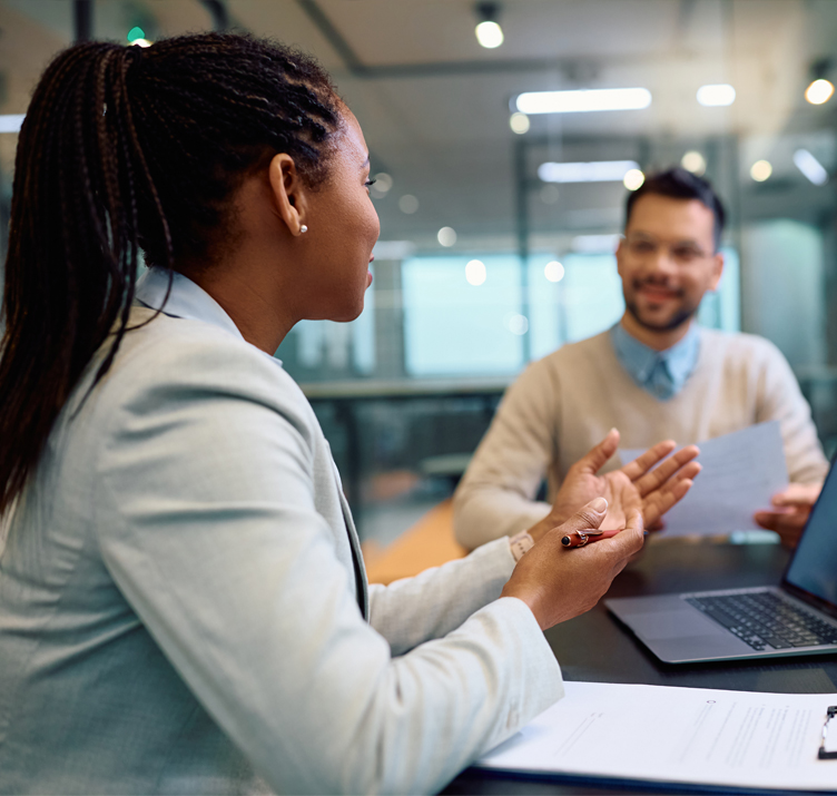 Young woman sitting at a conference table, actively talking and gesturing to a happy couple sitting across from her